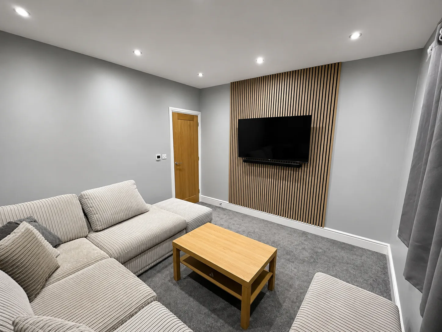 Living room — wood-slat feature wall, mounted TV and warm-neutral palette.