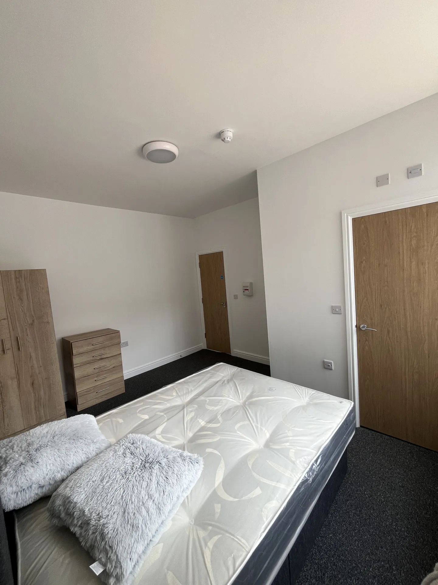 Ensuite bedroom — fitted wardrobe, dresser, double bed and natural light from a large window.